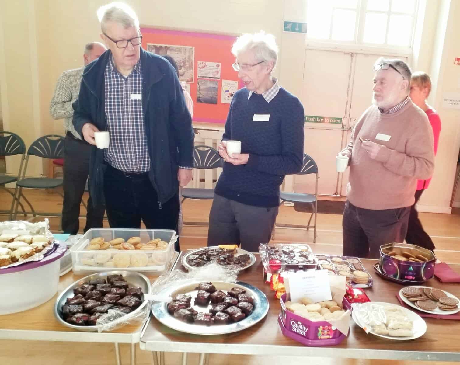Delighted Oriana Choir Macclesfield members enjoying tea and cookies during a social gathering.