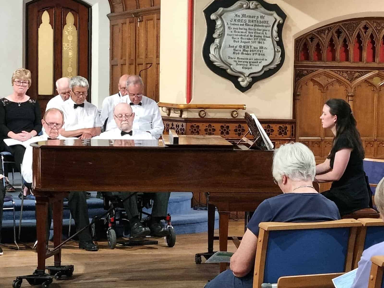 Vocal ensemble performing with pianist at Macclesfield Oriana Choir concert, showcasing choral music and community singing.