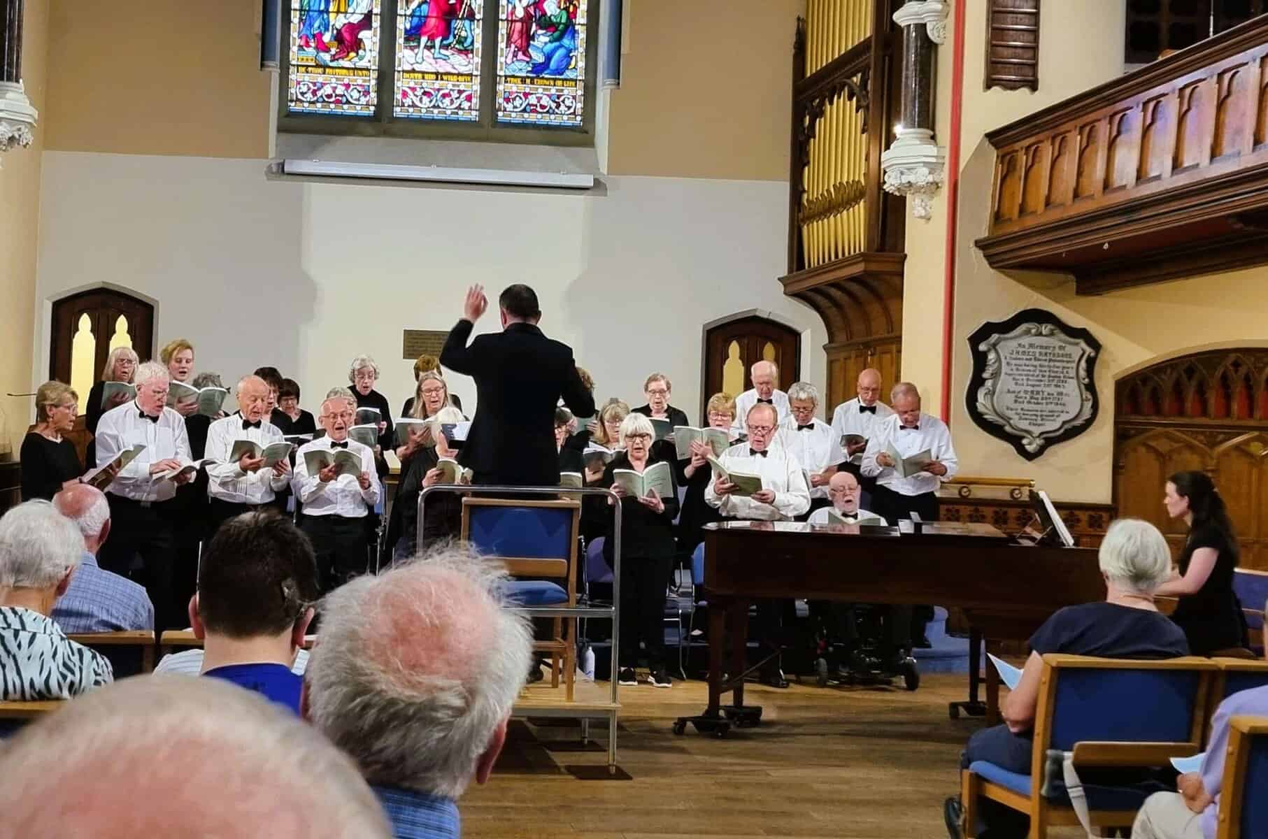 Oriana Choir Macclesfield performing in a church with stained glass windows.