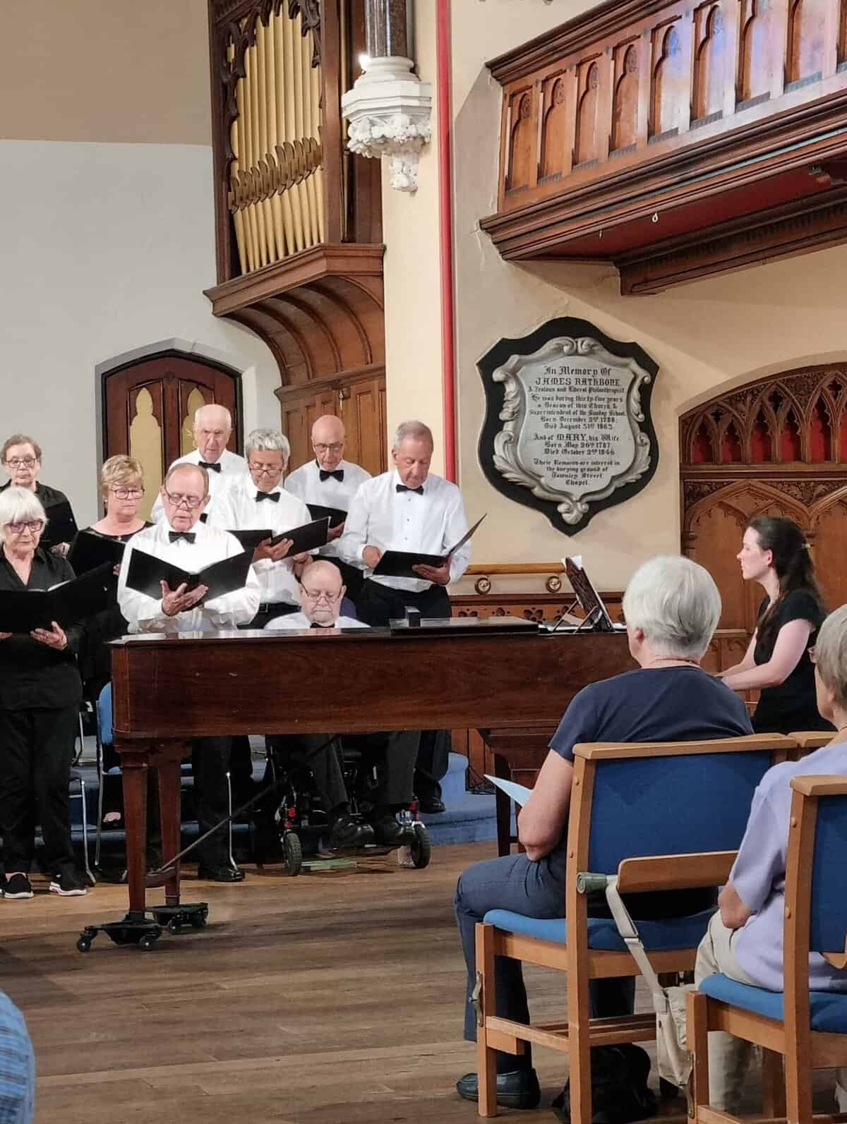 Oriana Choir Macclesfield performing in a church, showcasing a full choir with a pianist and attentive audience.