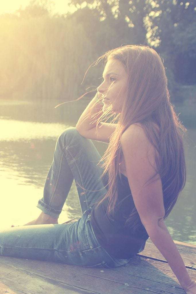 young woman sitting on a dock looking out at water at sunset manifesteveryday.com