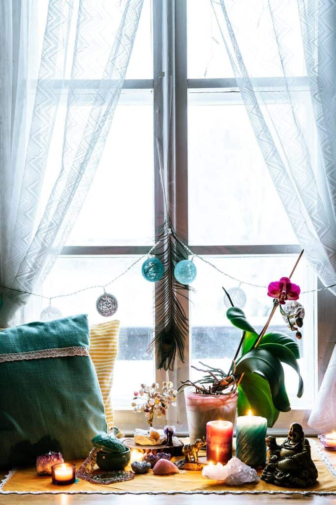 cozy, abundant boho scene of window, candles, plants, crystals, pillows and budhha