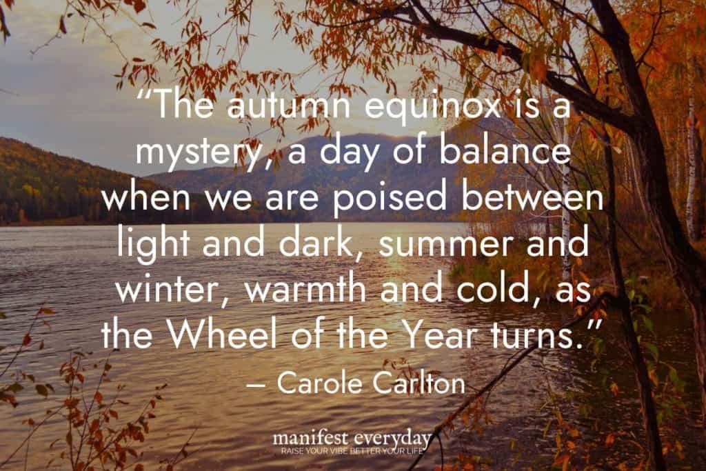 sunset over lake with fall colors with quote text that reads “The autumn equinox is a mystery, a day of balance when we are poised between light and dark, summer and winter, warmth and cold, as the Wheel of the Year turns.” - Carole Carlton manifesteveryday.com