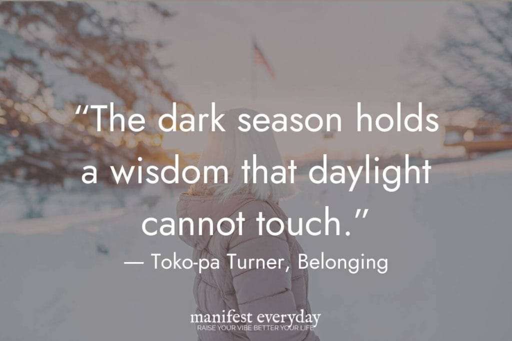 Person in winter puffer jacket against snowy bokeh background with quote 'The dark season holds a wisdom that daylight cannot touch' by Toko-pa Turner from Belonging. Quote image by manifesteveryday.com