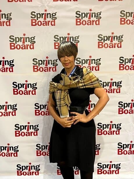 UOhnIt.com, woman standing in front of Spring Board background, fashionable outfit and scarf, event or conference attire, professional look.