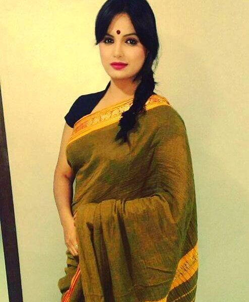 Beautiful woman in traditional Indian saree with black hair and red lipstick standing indoors.