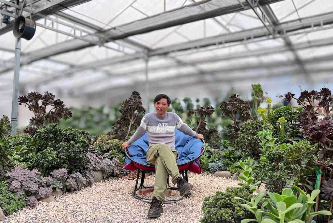 Hình ảnh Lê Văn Mép ngồi thư giãn trong nhà kính trồng rau sạch, thể hiện sự đam mê và kiến thức về.