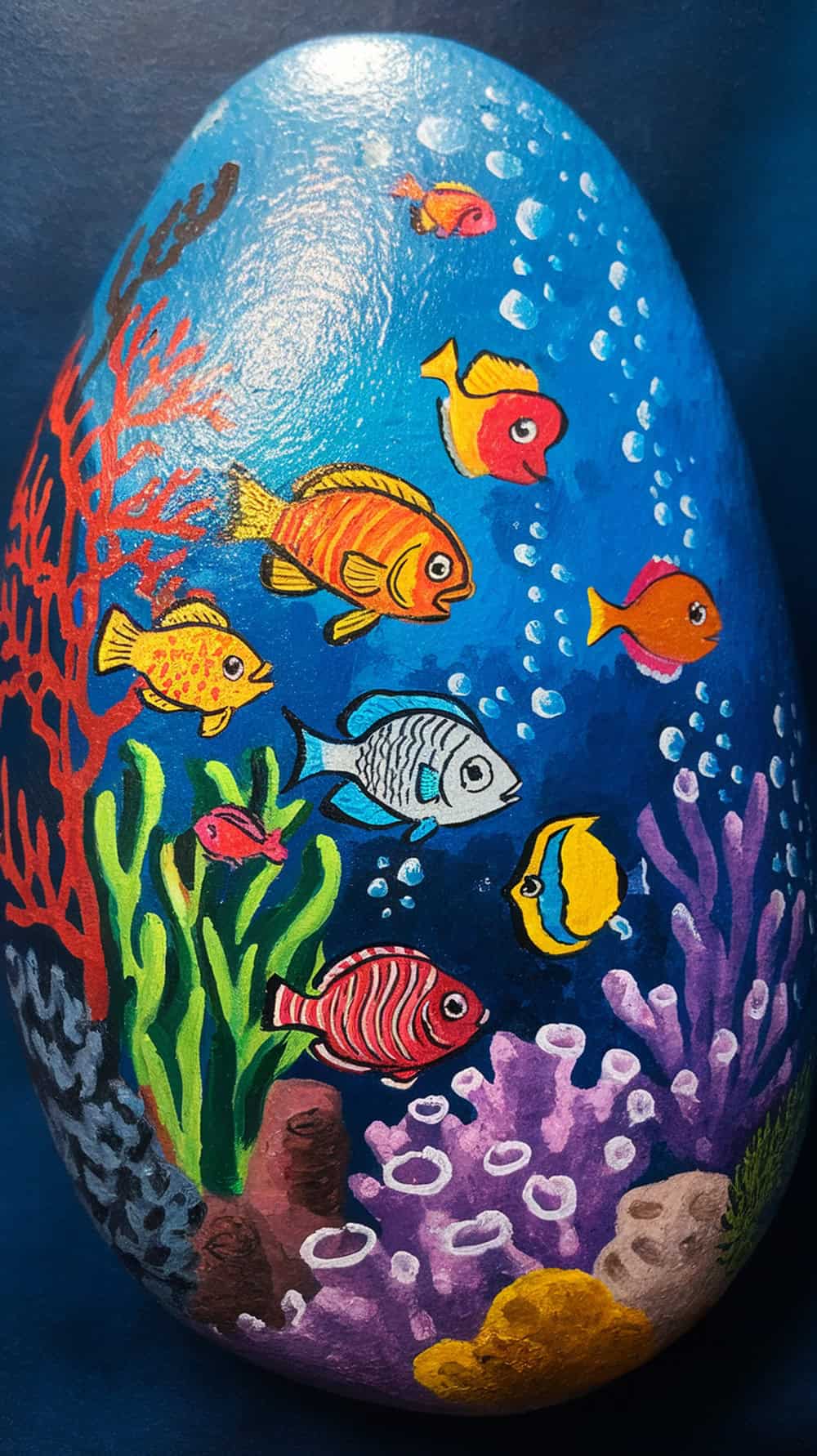 A painted rock featuring an underwater scene with colorful fish and coral.