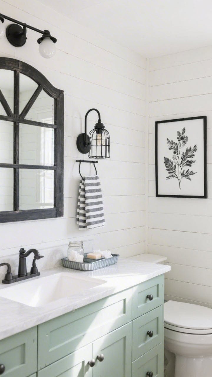 Wide shot, modern farmhouse bathroom: one wall clad in peel-and-stick shiplap, vanity painted soft sage with black barn-style mirror above; black cage sconce lighting, striped hand towels, galvanized tray corralling soaps, small mason jar for cotton pads; framed black botanical print on shiplap; bright, friendly daylight.