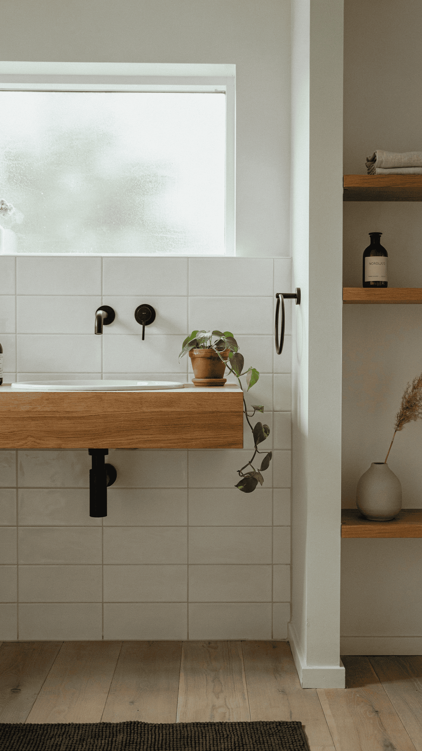 Warm gray Scandinavian bathroom with white tiles, oak accents, black fixtures, and minimalist styling.