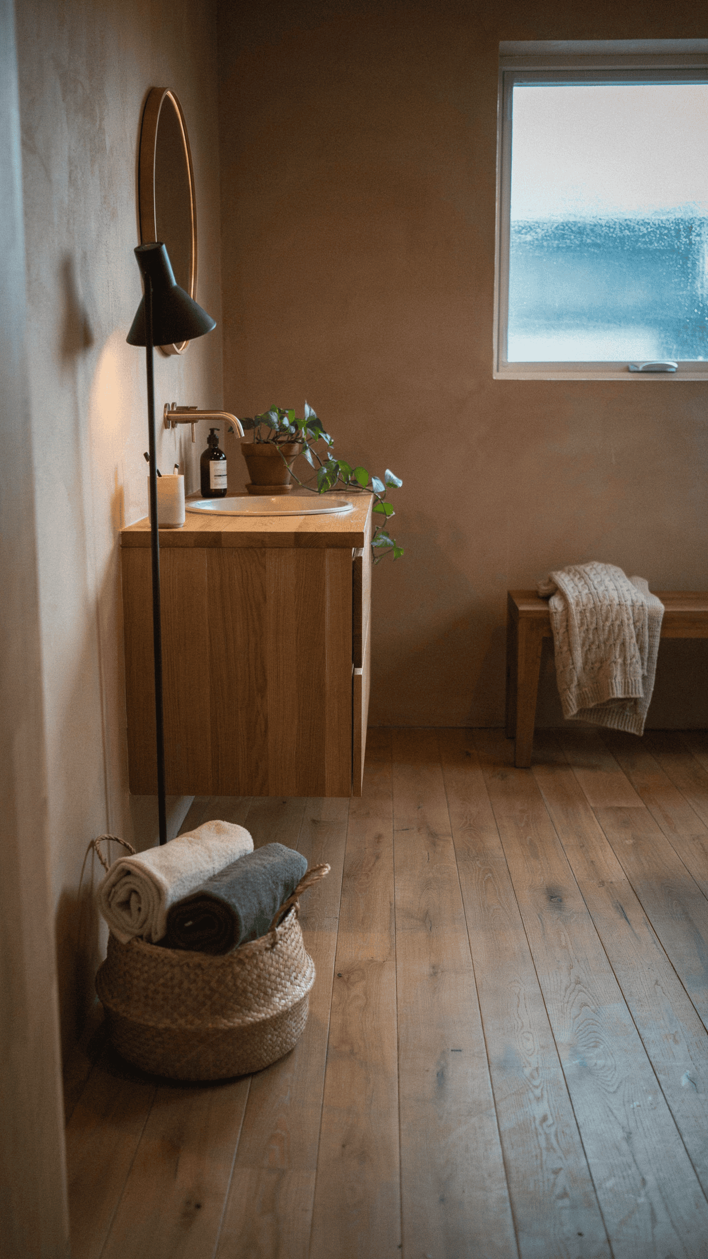 Scandinavian bathroom featuring pale clay walls, natural oak vanity, earthy textures, and warm ambient lighting.