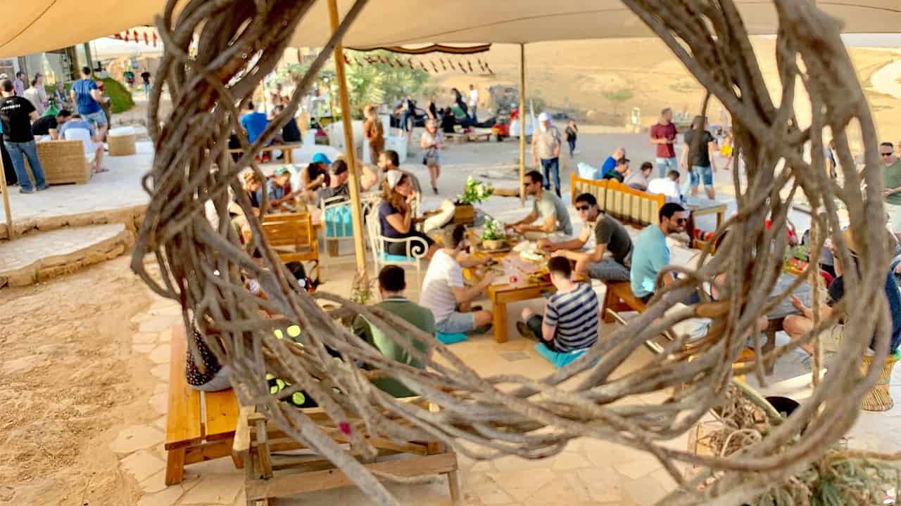 אורחים באירוע יושבים במדבר לצד שולחנות נמוכים