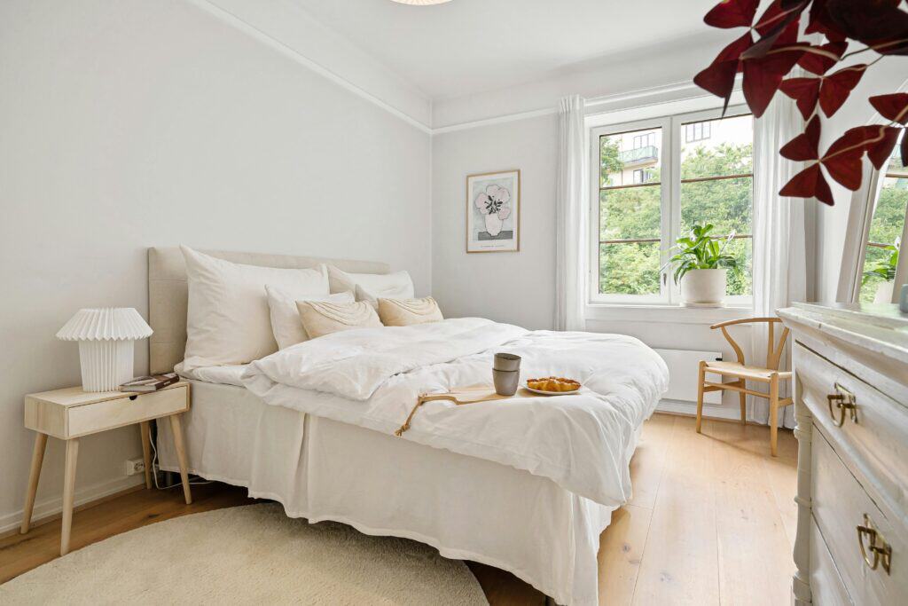 Bright and cozy bedroom interior with a breakfast setup on the bed and a view outside.