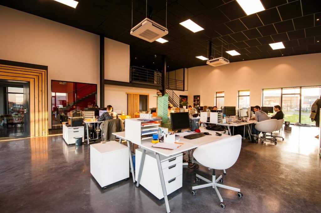 Modern open-plan office workspace with desks, computers and team collaboration in a large commercial interior.