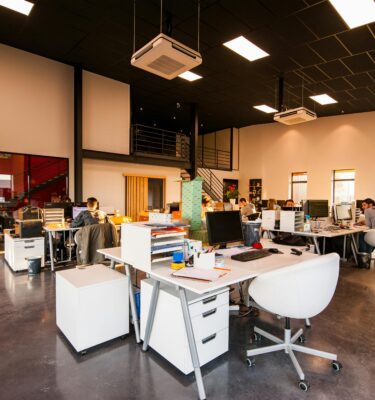 Modern open-plan office workspace with desks, computers and team collaboration in a large commercial interior.