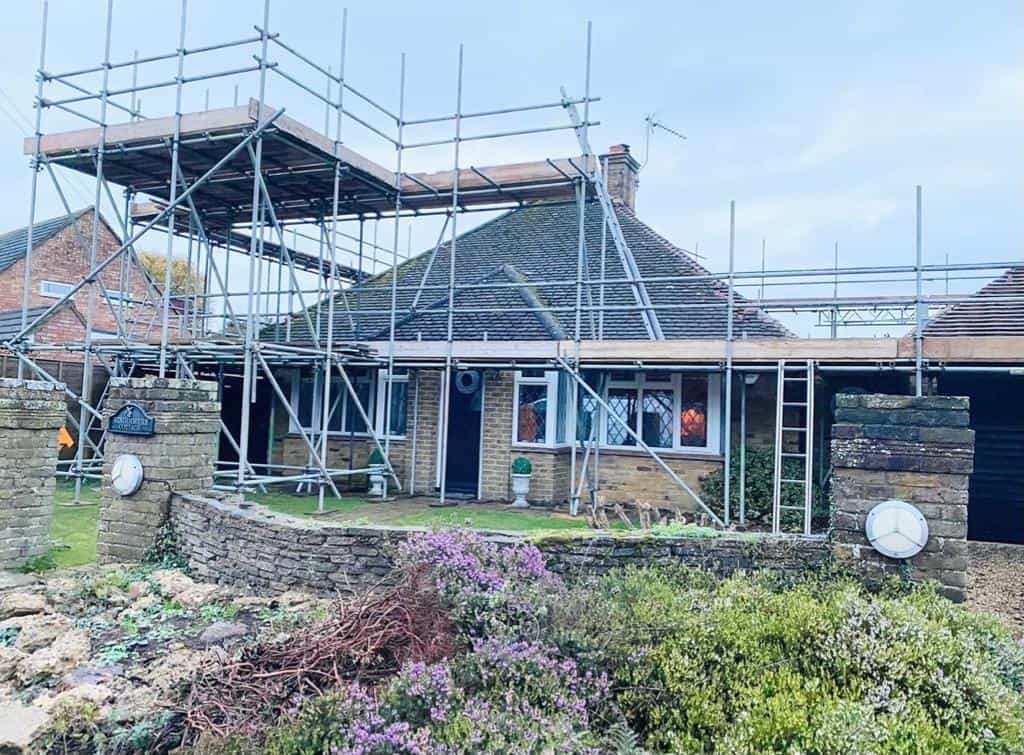 Residential house undergoing renovation with scaffolding and construction equipment.