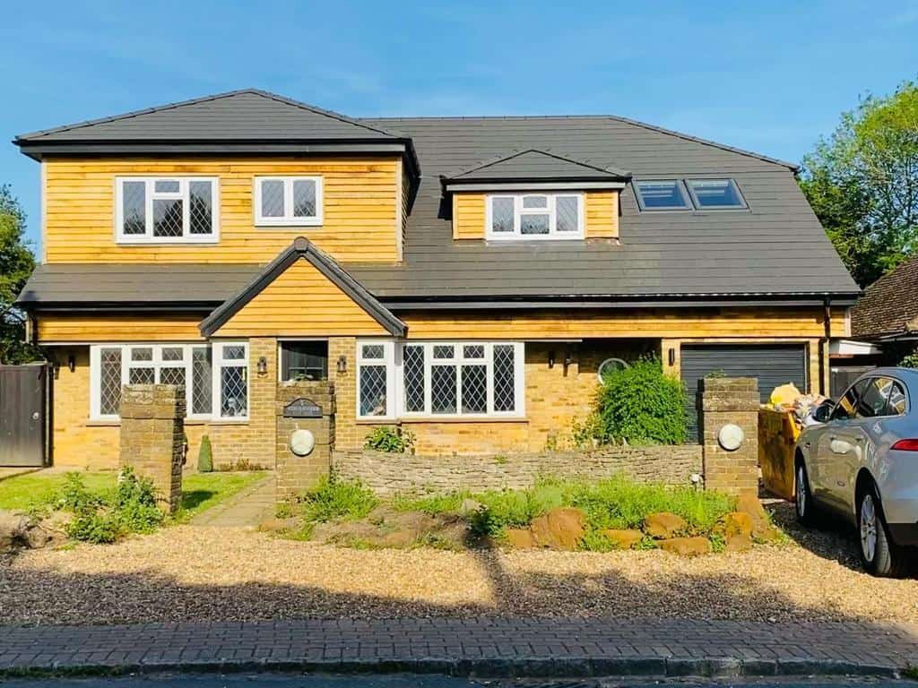 Contemporary detached house with yellow cladding and grey roof in a suburban setting.