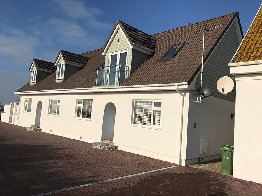 Contemporary house with dormer windows and white exterior in a sunny setting.
