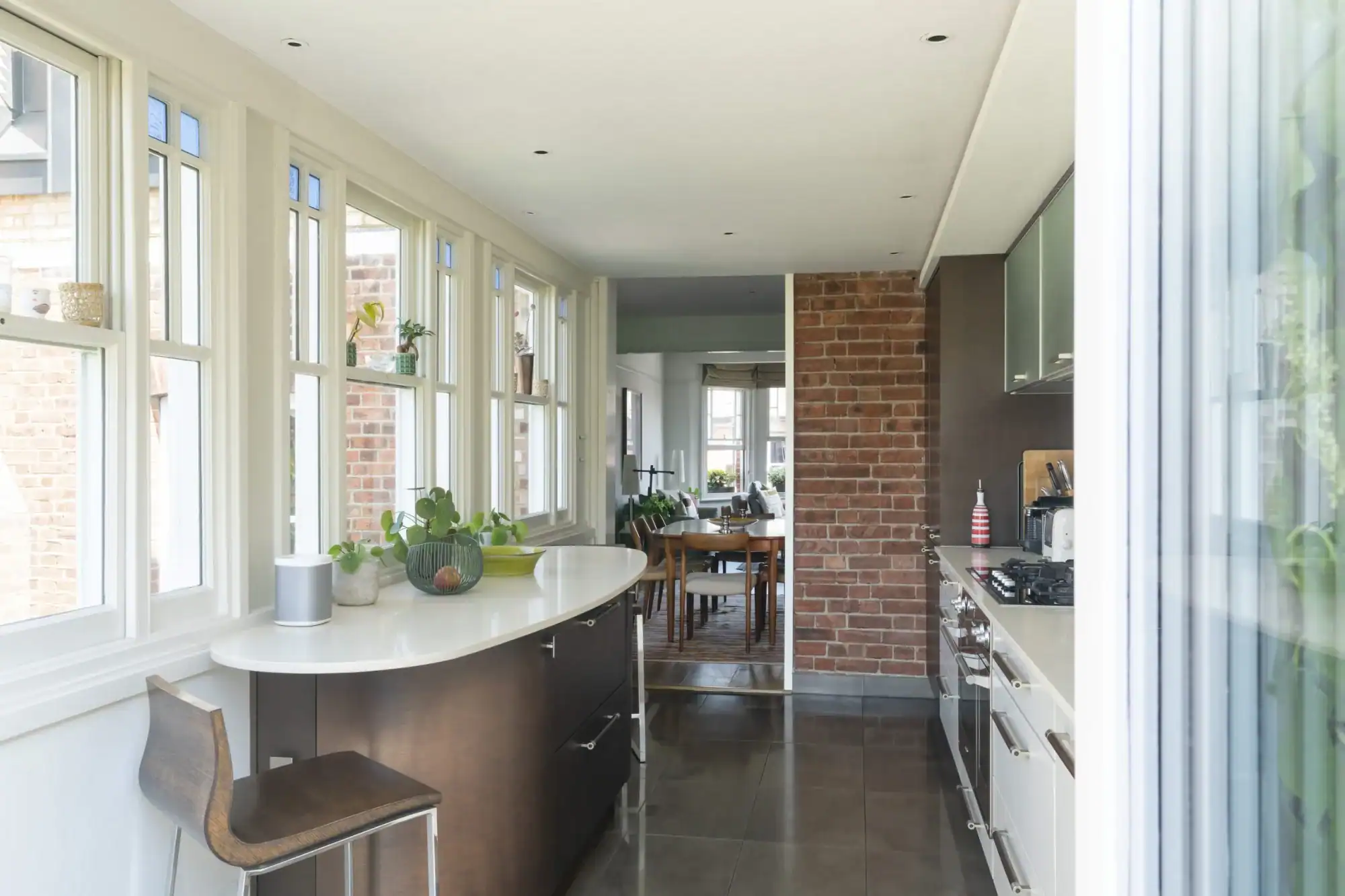 Bright modern kitchen with large windows and brick wall feature.