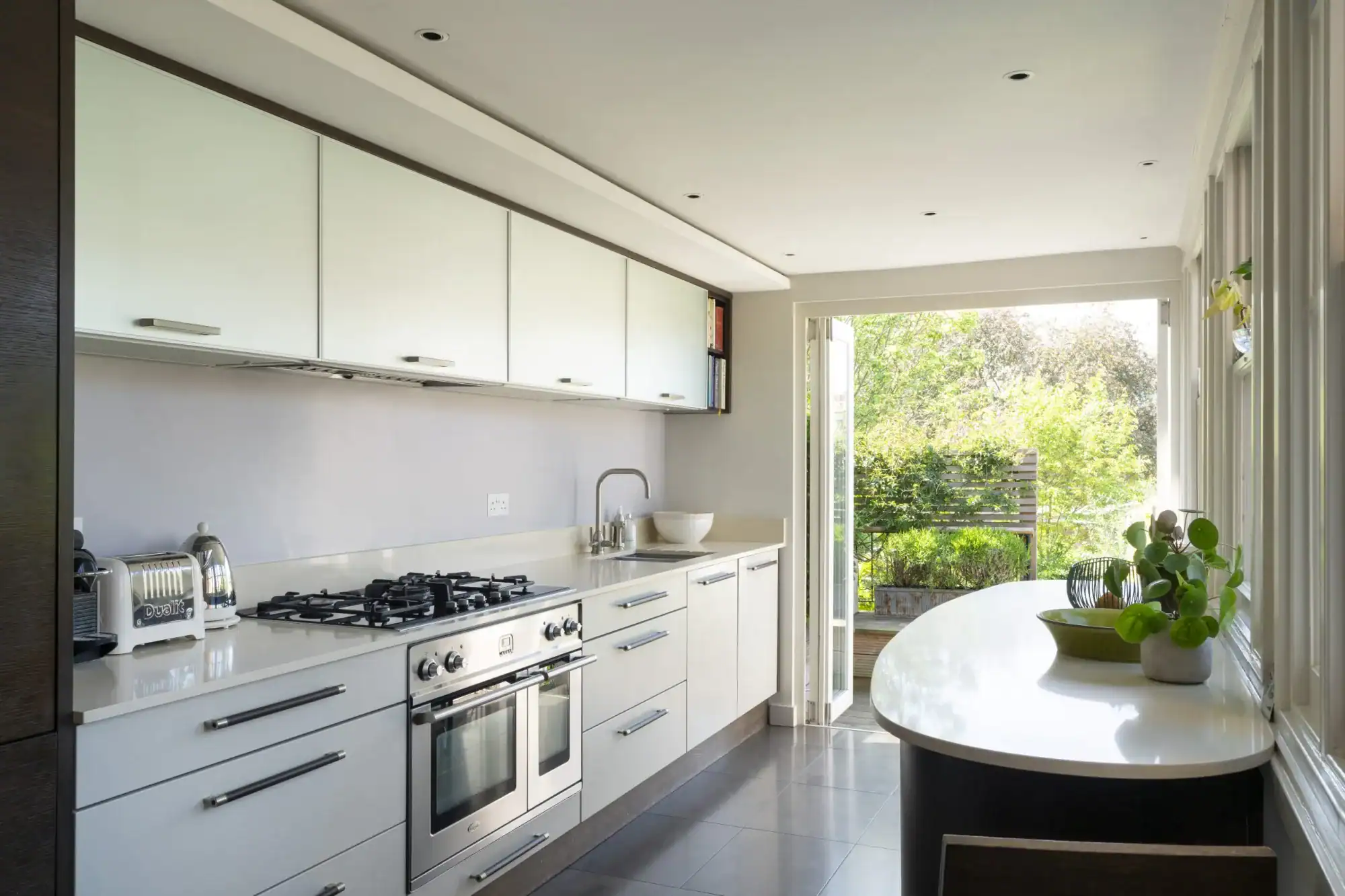 Modern white kitchen with large window and outdoor view.