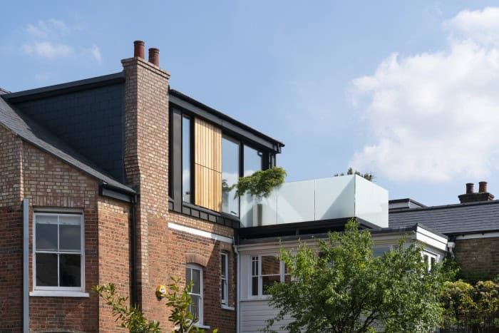 Modern rooftop extension on a traditional brick house with glass and wood features.