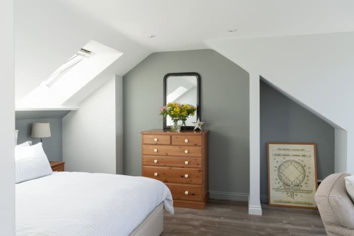 Bright attic bedroom with skylight, dresser, and decorative mirror.