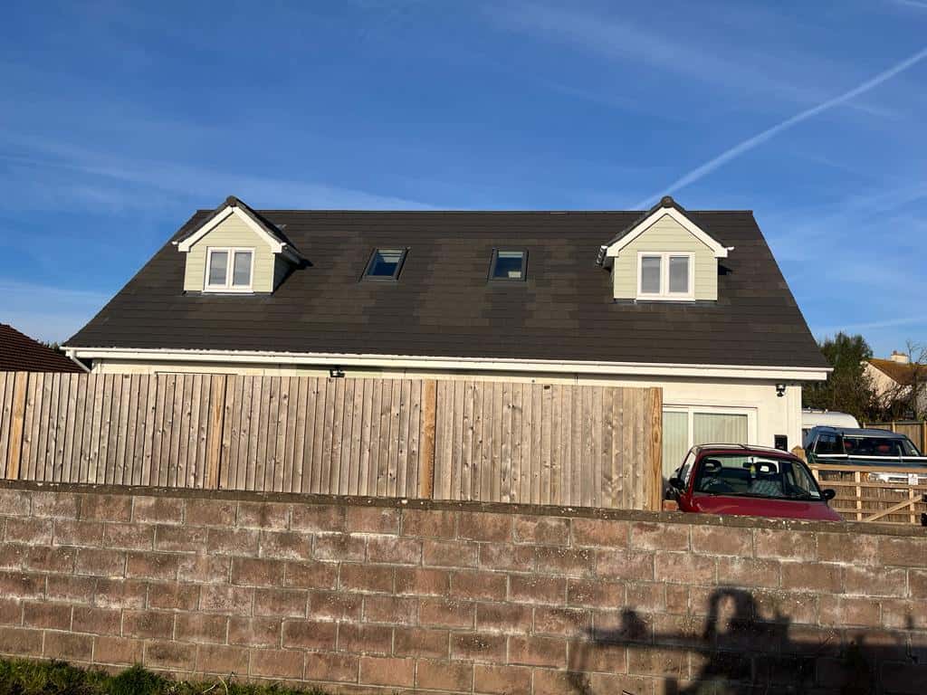 Modern house with dormer windows and a dark roof behind a wooden fence.