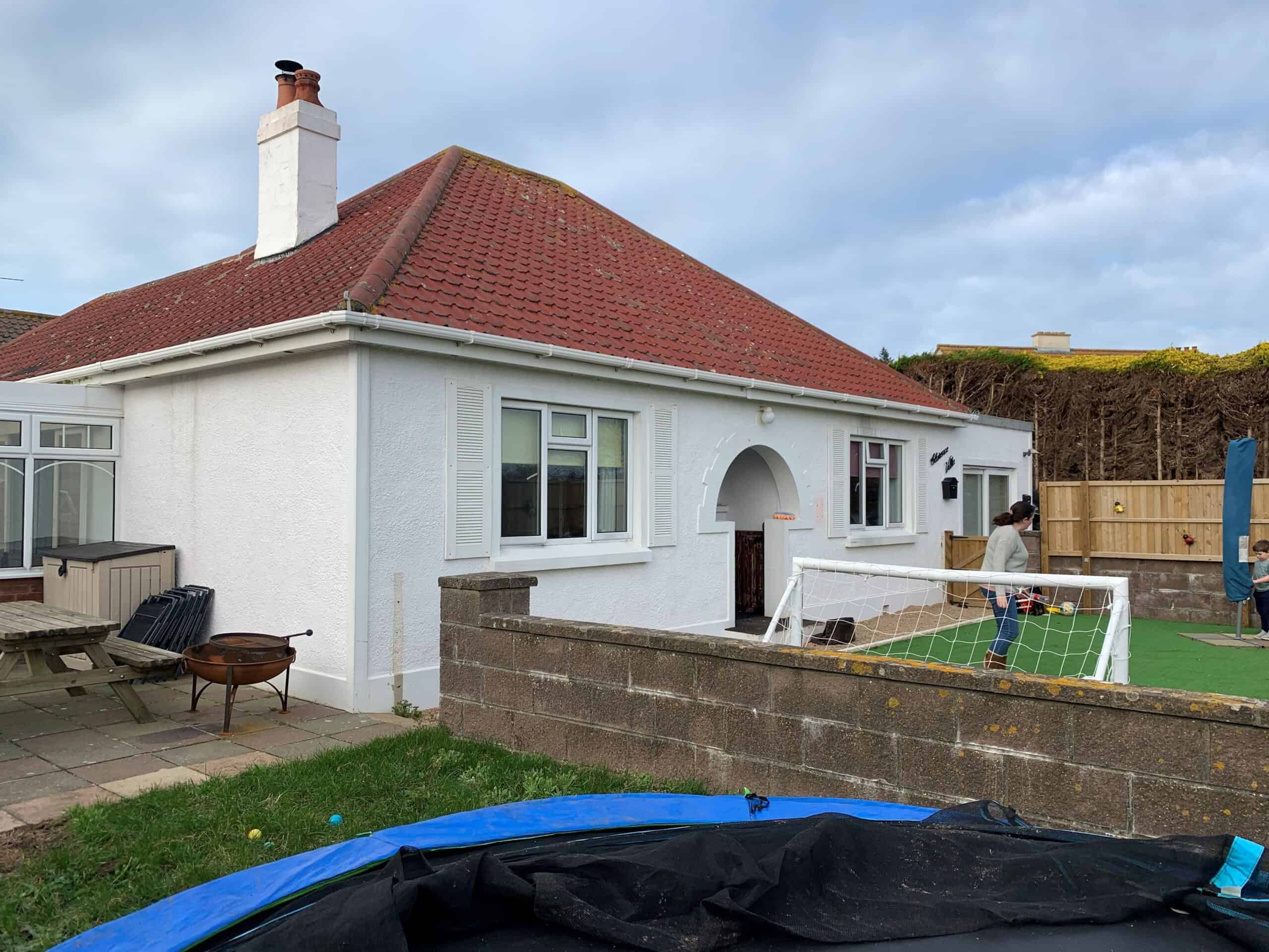 White house with red roof and garden, under renovation, with a small football pitch.