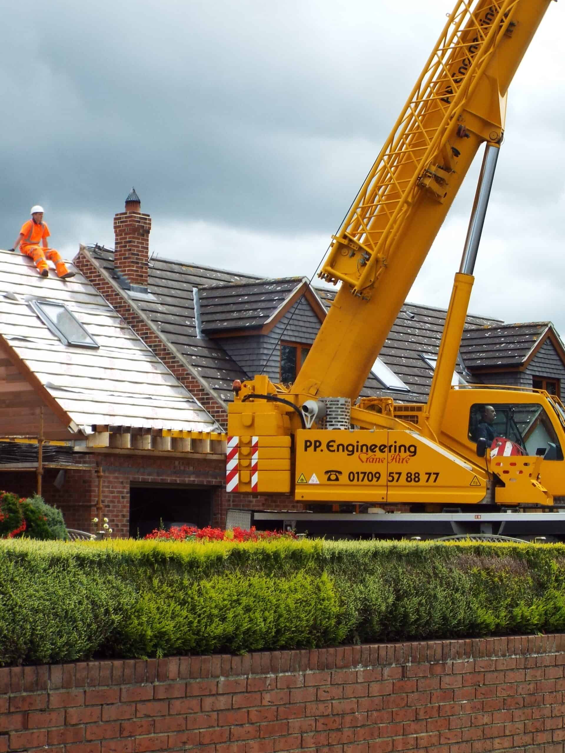 Roof repair work with a yellow crane and workers on a residential house.