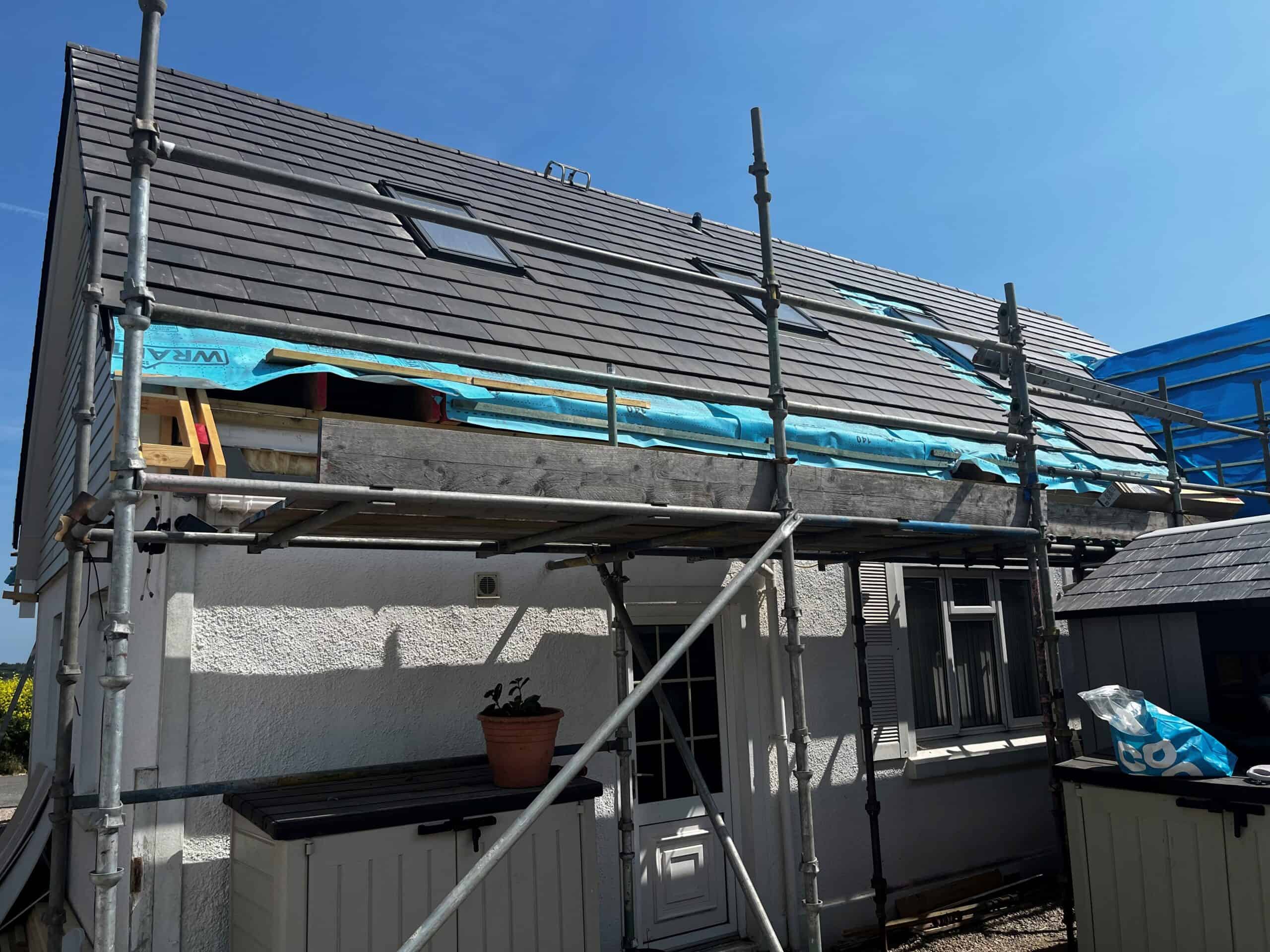 House under renovation with scaffolding and new roof installation in progress.