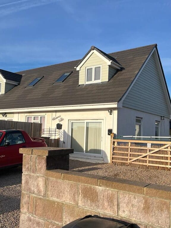 Modern house with a grey roof and white walls, featuring dormer windows and a garage.