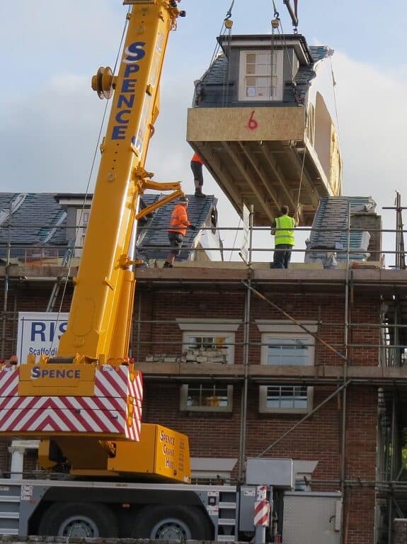 Modular home being lifted onto a building with a crane during construction.