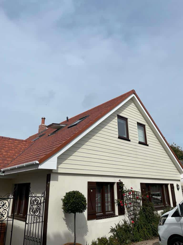Modern house with pitched roof and garden, featuring white siding and brown window frames.