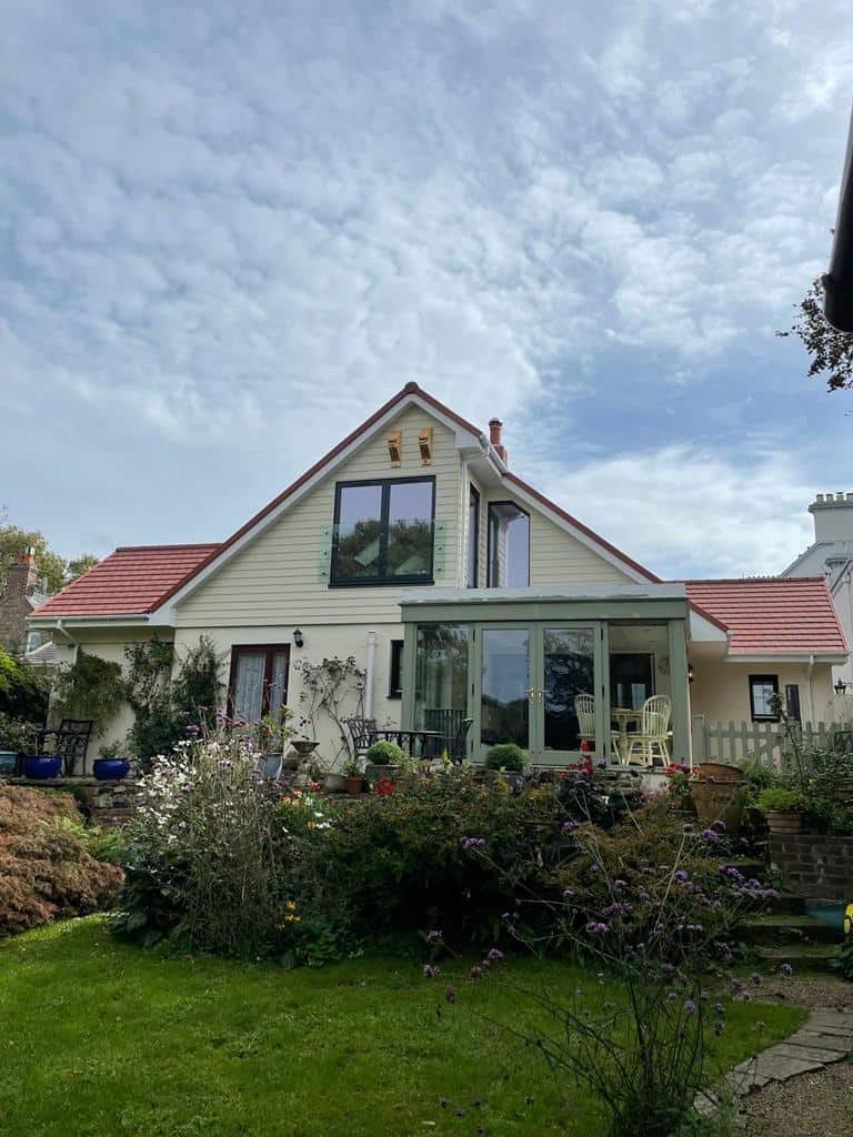 Modern house with large glass windows and a garden under a cloudy sky.