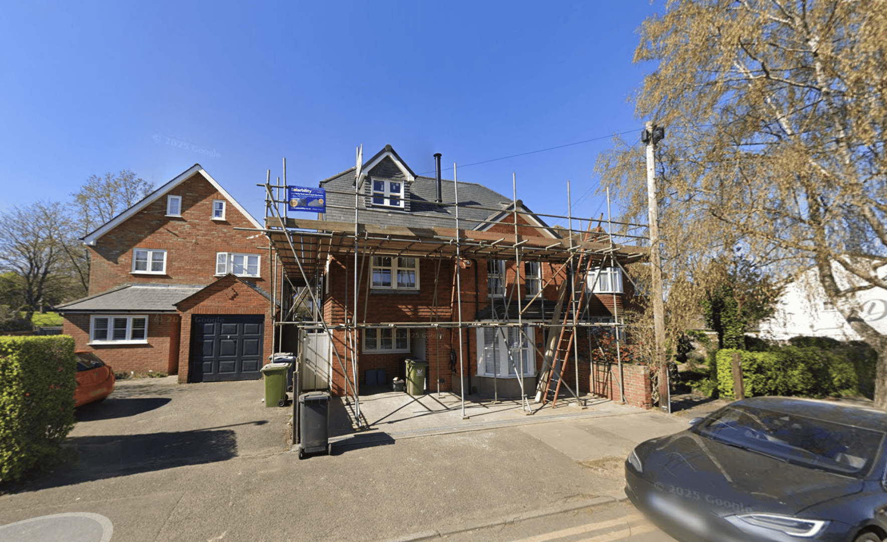 House under renovation with scaffolding and construction equipment in a residential area.