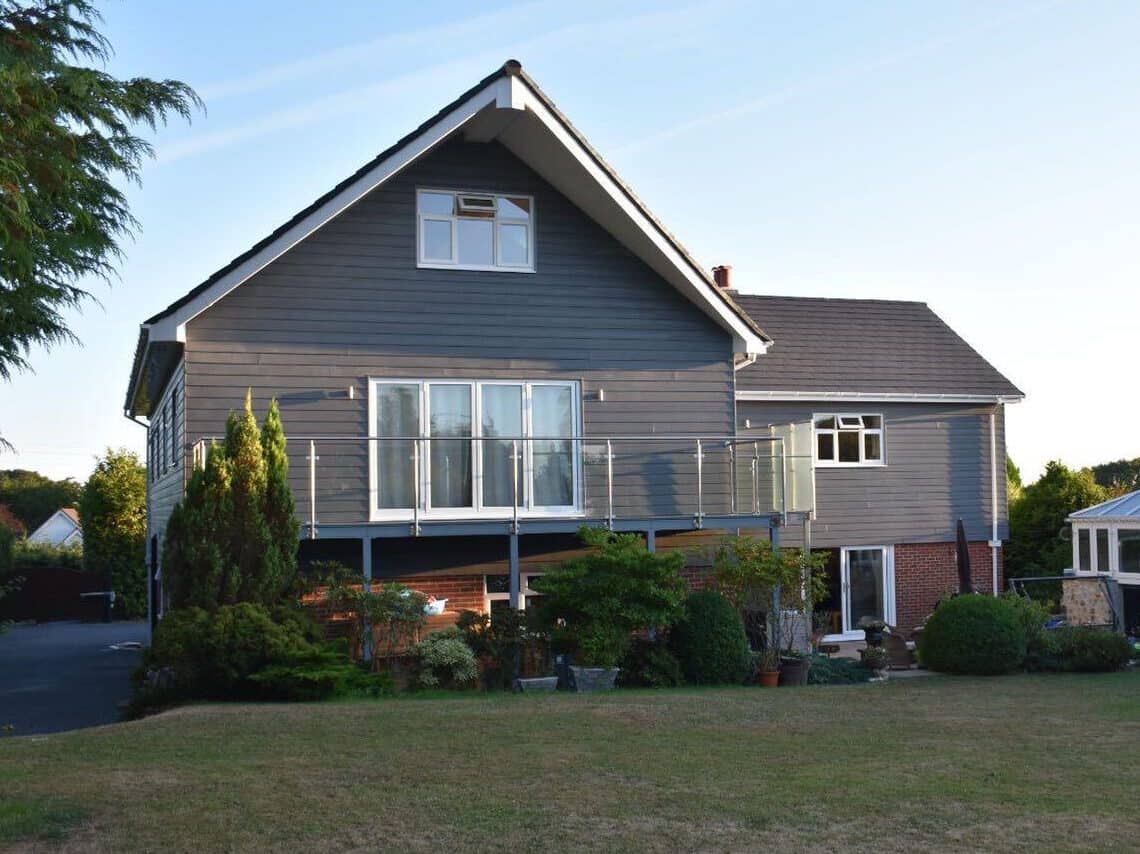 Modern grey house with balcony and garden, in a peaceful suburban setting.