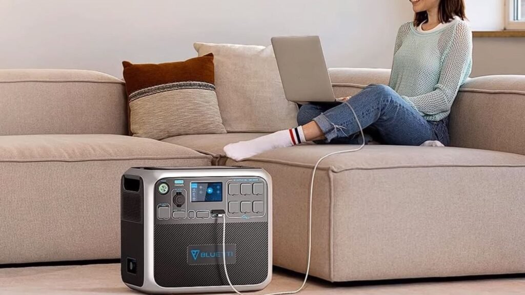 Une femme assise sur un canapé avec un ordinateur portable connecté à une station électrique portable.