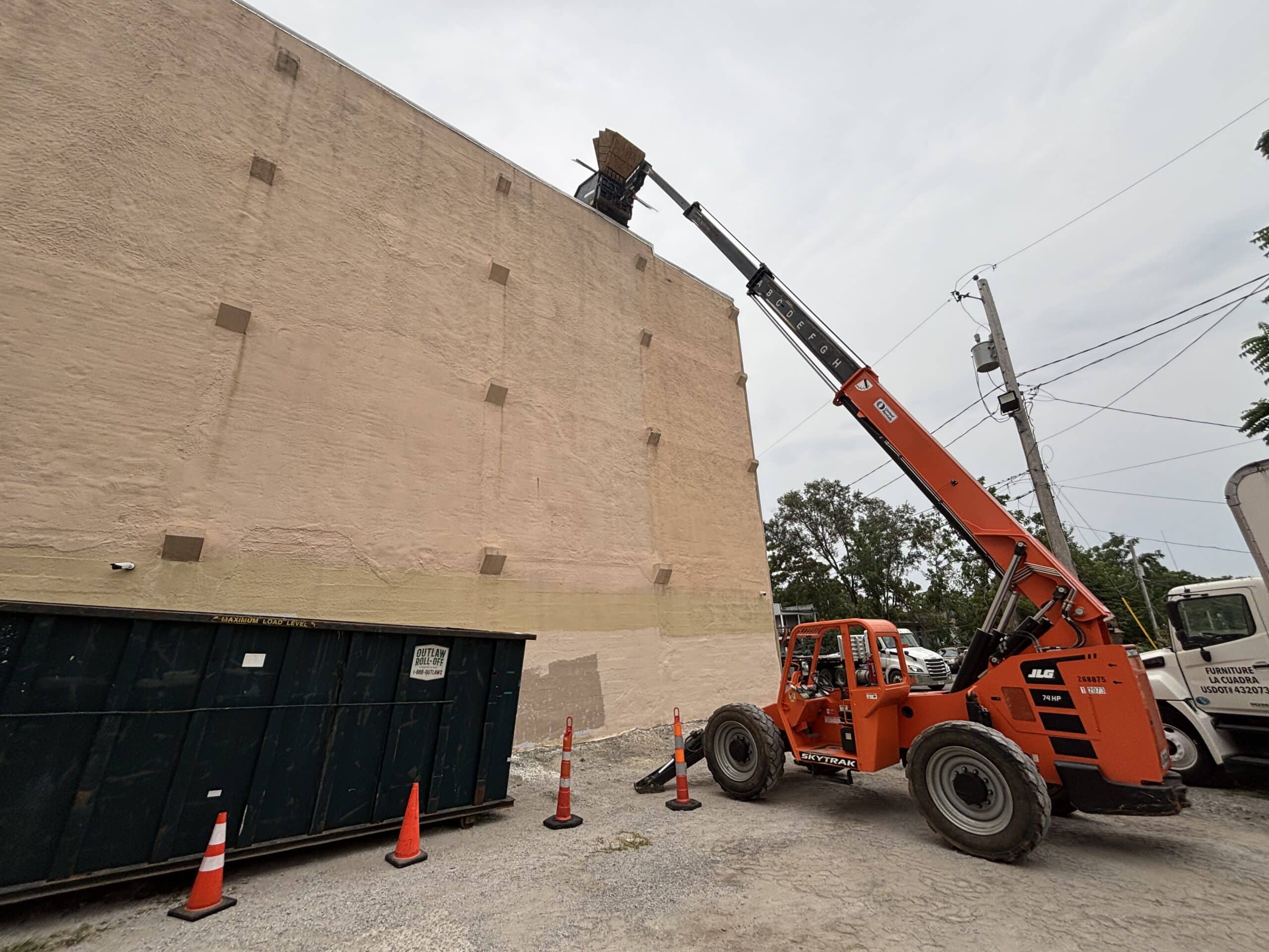 Roofing crane with lifting arm next to a building wall, used for roofing projects.