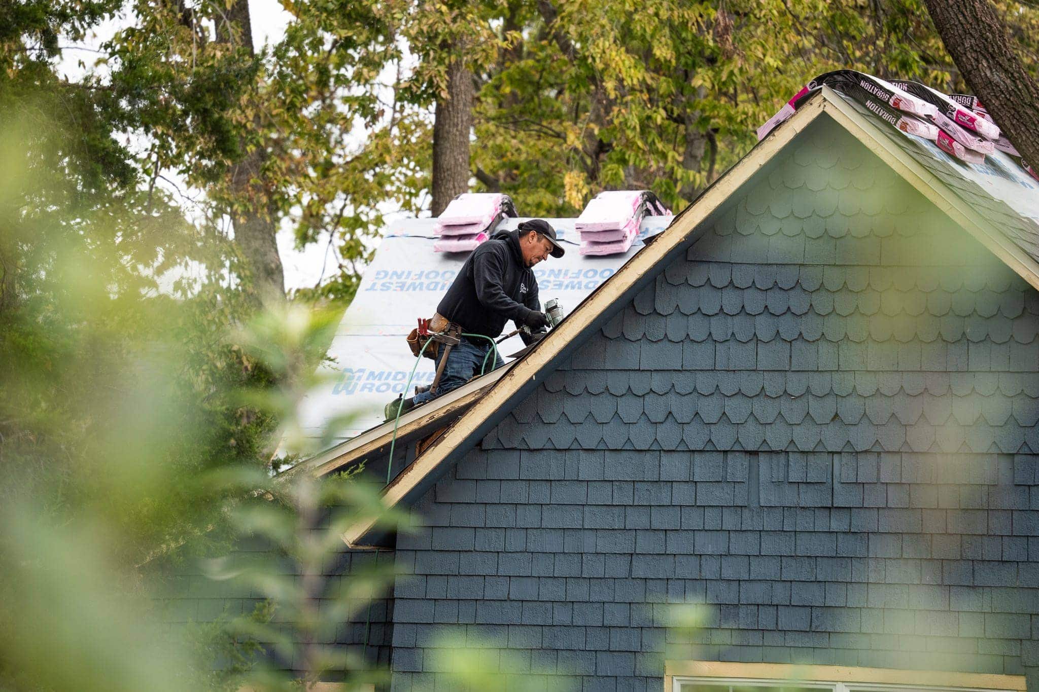 Roof repair by Midwest Roofing specialist installing new shingles on a residential home with greenish-blue siding.