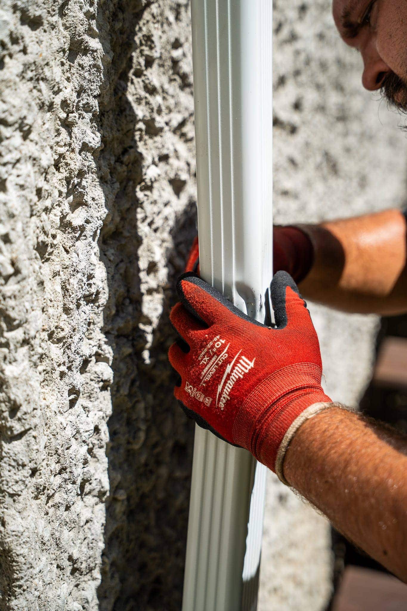 Roofing installation with a white gutter system on a textured exterior wall.