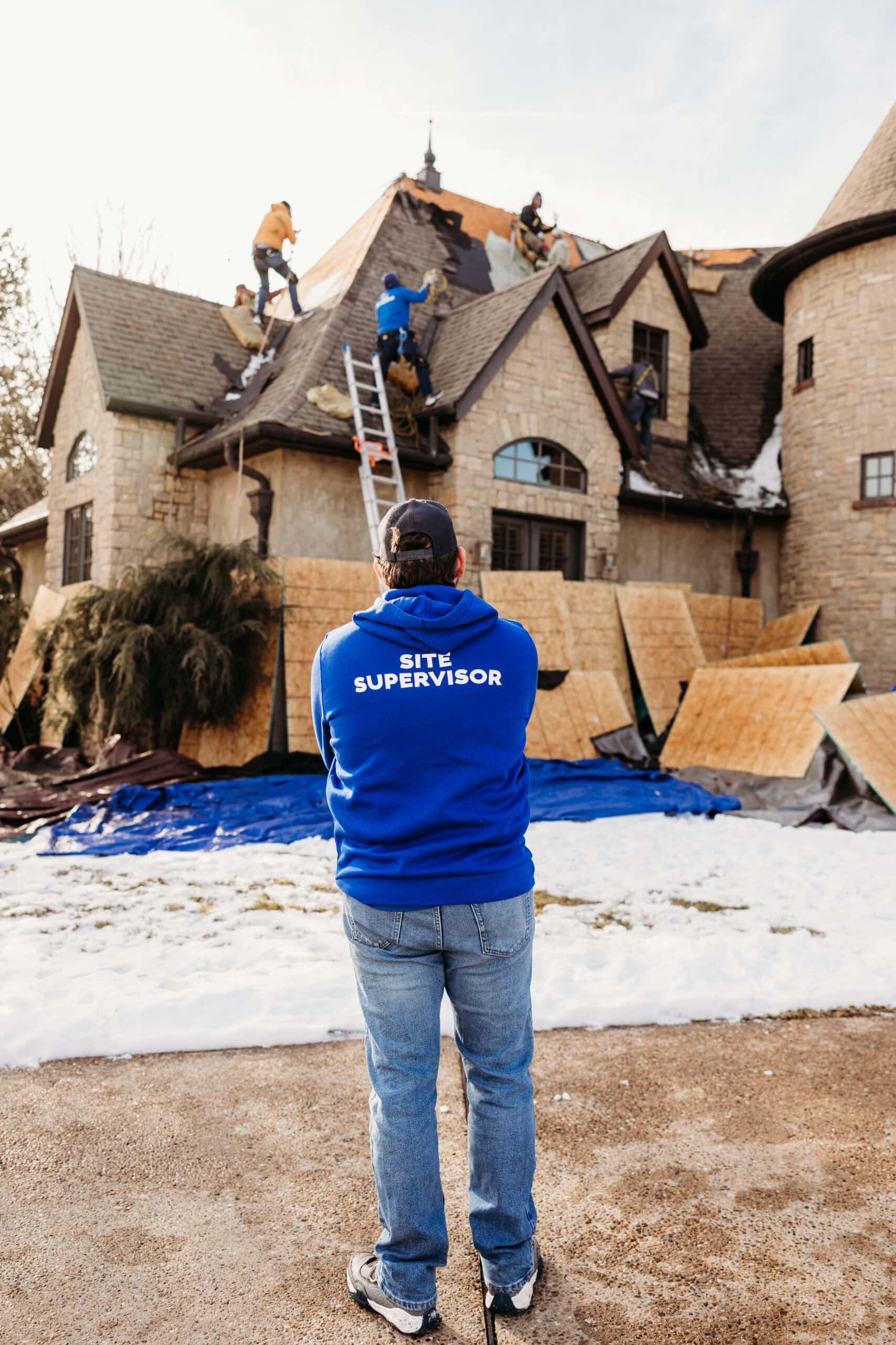 Roofing team installing new shingles on a large, multi-story house with steep roof angles.