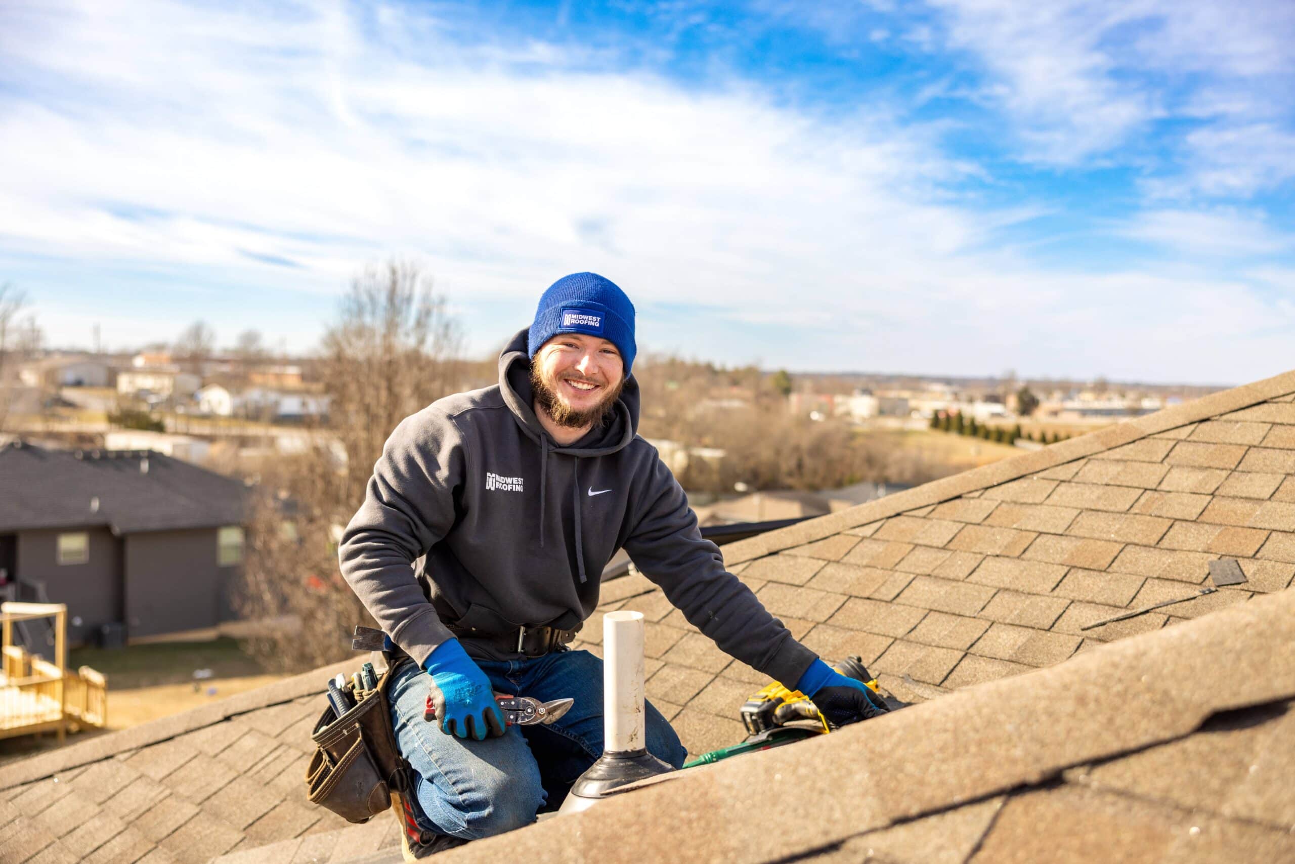 Roofing professional installing shingles on a residential roof in a suburban area.