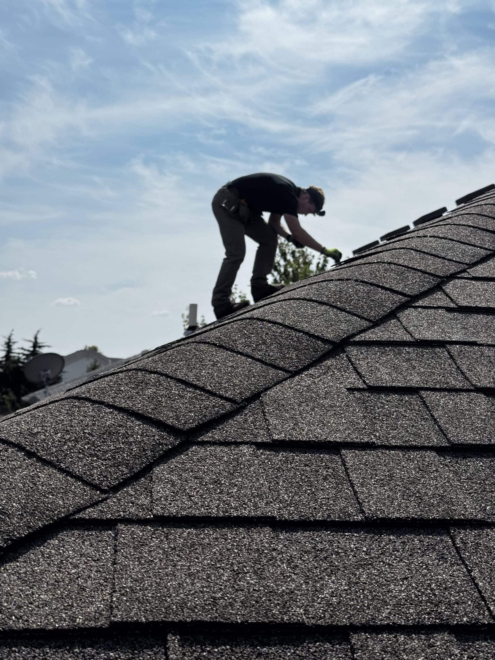 Roofing professional inspecting asphalt shingles on residential roof for damage or maintenance.