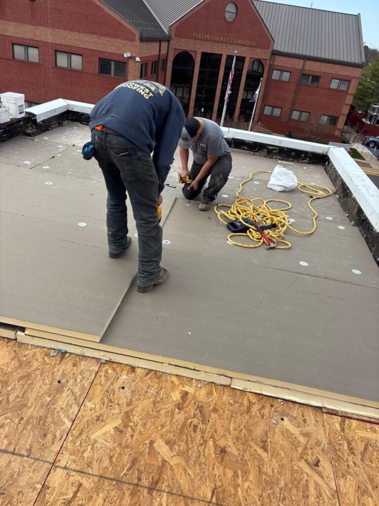Midwest Roofing crew fastening new insulation board on the museum roof, with the Phelps County Courthouse behind them