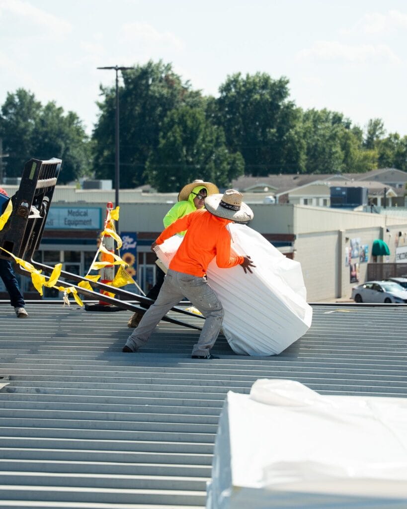 Midwest Roofing crew moving insulation board on a commercial metal roof deck in Sedalia, Missouri