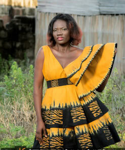 Robe batik couleur or et noire, évasée à double ovale superposées, manches asymétriques à volants, avec ceinture brodée.