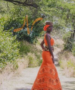 Robe longue brodée, en pagne tissé orange à brillantine or, Avec ceinture large brodée. Foulard et chapeau brodé assortis.