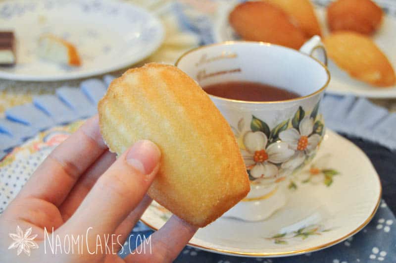 hand holding a madeleine with a teacup in the background