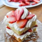 a square mini strawberry shortcake on a glass plate on a cutting board with strawberries in the background