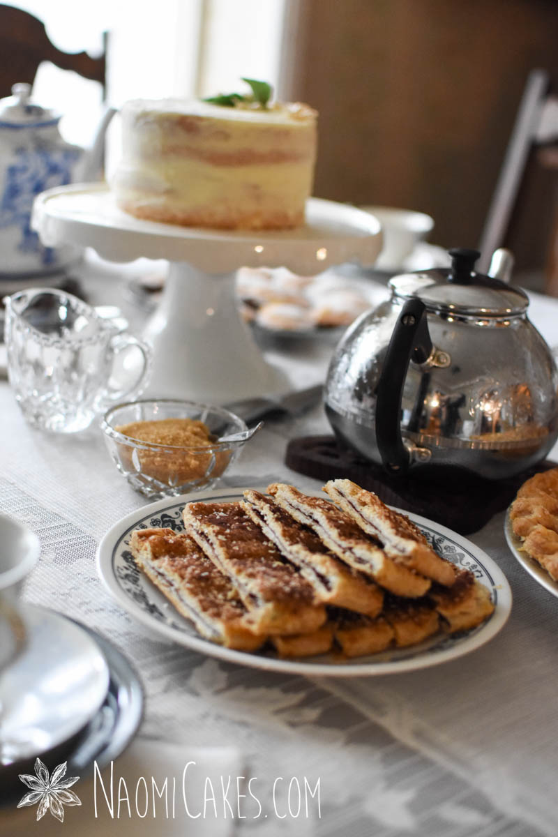 plate of cinnamon sprinkled baked pastry on a table with a tea pot and cake in the background